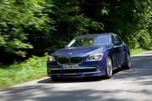 Синий BMW 7 series проезжает по летней лесной трассе